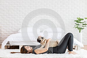 Beautiful Asian young woman playing with her dog and smile with dog pug breed looking in funny and serious face in bedroom
