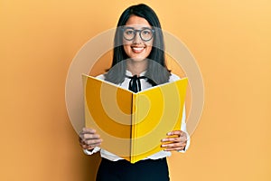 Beautiful asian young woman reading a book wearing glasses smiling with a happy and cool smile on face