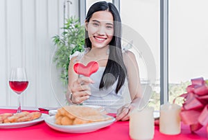 Beautiful asian young woman sitting and happy smiling with showing red heart shaped in restaurant