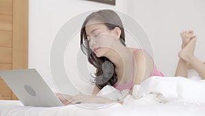 Beautiful asian young woman smiling lying on bed using laptop computer at bedroom for leisure