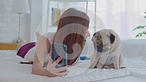 Beautiful Asian young woman take a photo selfie bu mobile phone with her cute dog pug breed in cozy bedroom,Happiness girl playing