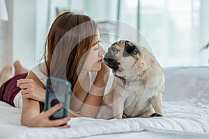Beautiful Asian young woman take a photo selfie bu mobile phone with her cute dog pug breed in cozy bedroom,Happiness girl playing
