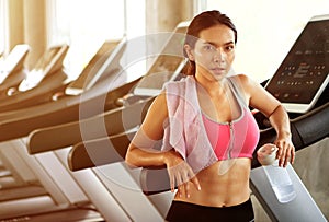 Beautiful Asian young woman tired taking a break from running or exercise standing on treadmill machine drinking water and towel