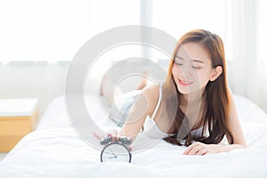 Beautiful asian young woman turn off alarm clock in morning, wake up for sleep with alarm clock.