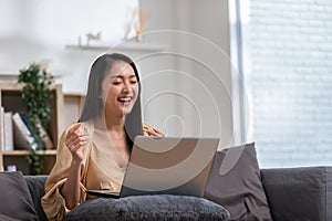 Beautiful asian young woman wear casual sit on couch using computer laptop entertain with social media relax smile and laughing.