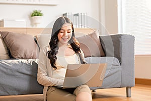 beautiful asian young woman wear casual sit on couch using computer laptop entertain with social media relax smile and laughing.