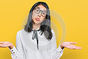 Beautiful asian young woman wearing business shirt and glasses clueless and confused expression with arms and hands raised