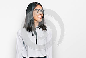 Beautiful asian young woman wearing business shirt and glasses looking away to side with smile on face, natural expression