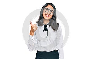 Beautiful asian young woman wearing business shirt and glasses smiling happy and positive, thumb up doing excellent and approval