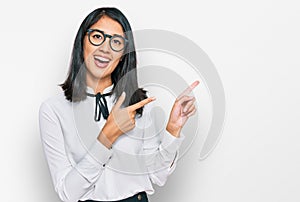 Beautiful asian young woman wearing business shirt and glasses smiling and looking at the camera pointing with two hands and