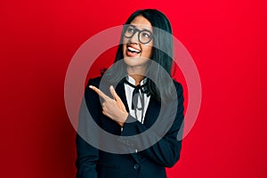 Beautiful asian young woman wearing business suit cheerful with a smile of face pointing with hand and finger up to the side with