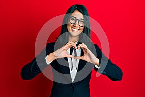 Beautiful asian young woman wearing business suit smiling in love doing heart symbol shape with hands