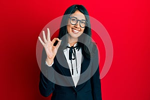 Beautiful asian young woman wearing business suit smiling positive doing ok sign with hand and fingers