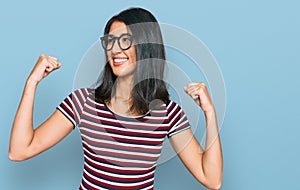 Beautiful asian young woman wearing casual clothes and glasses showing arms muscles smiling proud
