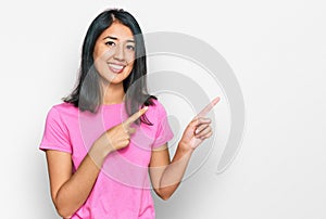 Beautiful asian young woman wearing casual pink t shirt smiling and looking at the camera pointing with two hands and fingers to