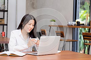 Beautiful asian young woman working online on laptop sitting at coffee shop