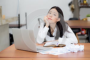 Beautiful asian young woman working online problem with laptop and think project and paper crumpled on table.