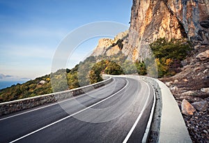 Beautiful asphalt road in autumn forest at sunrise. Mountains