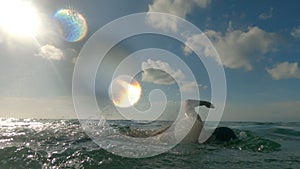 A beautiful athlete swimmer technically swims in the ocean in the rays of sunlight. The silhouette of a swimmer rowing