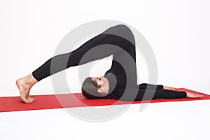 Beautiful athletic girl in black suit doing yoga. halasana asana - plow pose. Isolated on white background. photo
