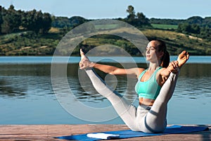 Beautiful athletic girl doing Ashtanga Vinyasa Asana Upavishtha Konasana outdoors against beautiful nature in the morning