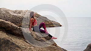 Beautiful athletic girl in sportswear sitting on a rock in the midst of the sea ha the background of beautiful scenery