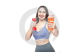 A beautiful, athletic, slim, smiling and cheerful woman holds a red dumbbell and a shaker with water. Lifestyle concept