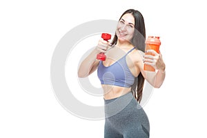 A beautiful, athletic, slim, smiling and cheerful woman holds a red dumbbell and a shaker with water. Lifestyle concept