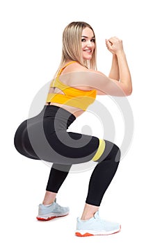 A beautiful, athletic, slim, smiling and cheerful woman in an orange top and black sweatpants performs squats with a