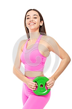 A beautiful, athletic, slim, smiling and cheerful woman in a pink tracksuit holds a green barbell pancake in her hands