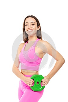 A beautiful, athletic, slim, smiling and cheerful woman in a pink tracksuit holds a green barbell pancake in her hands
