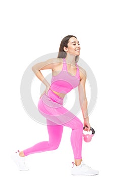 A beautiful, athletic, slim, smiling and cheerful woman in a pink tracksuit performs exercises with a pink kettlebell