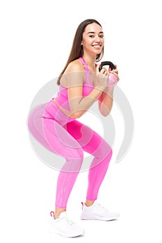 A beautiful, athletic, slim, smiling and cheerful woman in a pink tracksuit performs squats with a pink kettlebell