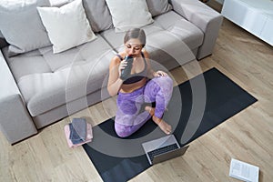 Beautiful Athletic Sporty Woman Sitting On Yoga Mat After Some Exercises Drinks Protein Shake or water