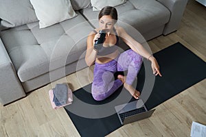 Beautiful Athletic Sporty Woman Sitting On Yoga Mat After Some Exercises Drinks Protein Shake or water