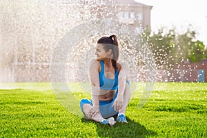 Beautiful, athletic woman with a muscular pumped up body sitting on the grass in urban football stadium. Posing, smiling happily