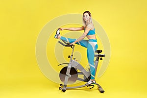 Beautiful athletic woman stretching leg before workout on exercise bike, looking away.