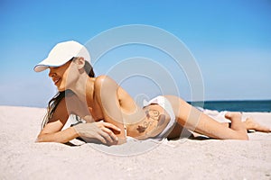 Beautiful athletic woman tanning in bikini on sandy beach at summer. Summer vacation concept.