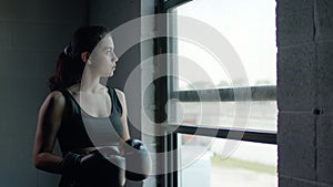 Beautiful athletic woman training boxing in the gym, putting on gloves and standing by the window.