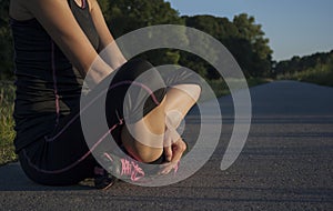 Beautiful athletic young adult woman is taking a break during outdoor exercising, sitting cross legged