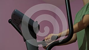 Beautiful athletic young girl on an elliptical trainer in the gym. Concept. Side view of a woman doing sport exercise on