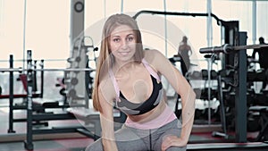 Beautiful athletic young girl trains dumbbells biceps in the gym.