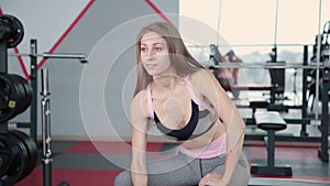 Beautiful athletic young girl trains dumbbells biceps in the gym.