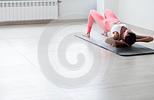 Beautiful athletic young woman in fashionable fit wear using foam roller in gym to workout to remove back pain, stretching and