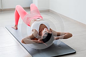 Beautiful athletic young woman in fashionable fit wear using foam roller in gym to workout to remove back pain, stretching and