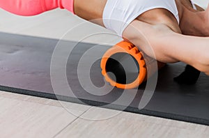 Beautiful athletic young woman in fashionable fit wear using foam roller in gym to workout to remove back pain, stretching and