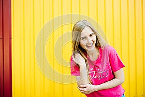 Beautiful athletic young woman with long blond hair in pink shirt and blue jeans. Posing and smiling at wall of the garage on