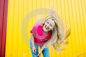 Beautiful athletic young woman with long blond hair in pink shirt and blue jeans. Posing and smiling at wall of the garage on