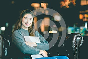 Beautiful Attractive Asian Business woman wearing sweater smile and hug computer laptop on sofa in coffee shop