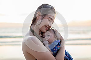 Beautiful Attractive Asian mom holding her baby newborn in hand and hugging baby sweet and lovely outdoor on the beach.Happy